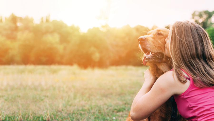Lauke sėdinti moteris ir bučiuojanti savo šuns snukutį